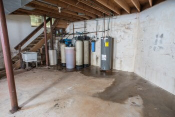 Inside an unfinished basement with a puddle of water on the floor